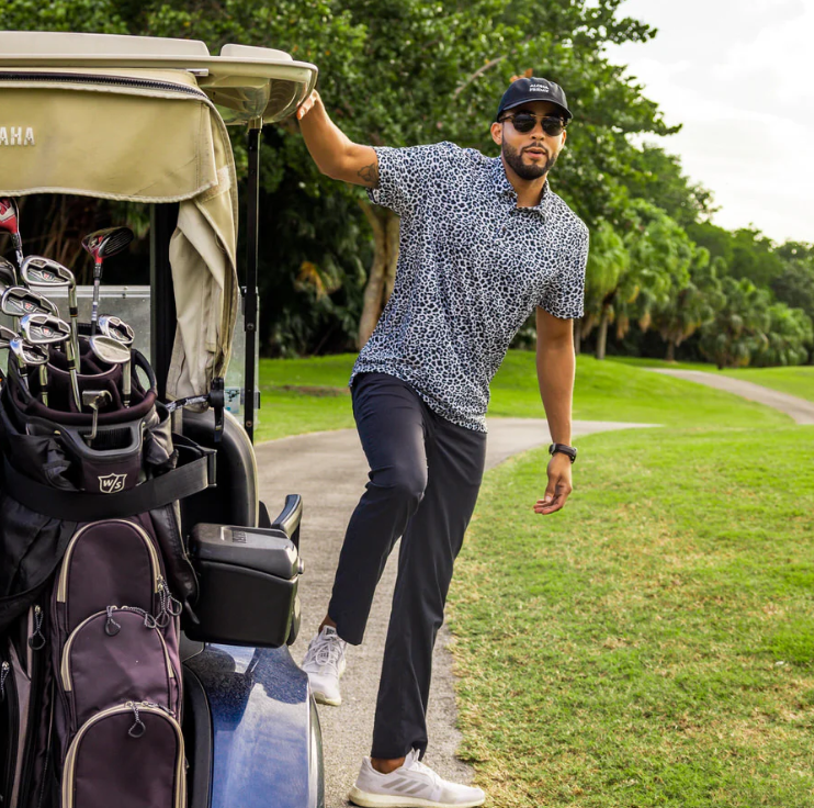 Man står på sidan av en golfbil med svarta byxor svartvit golfpiké och svart keps